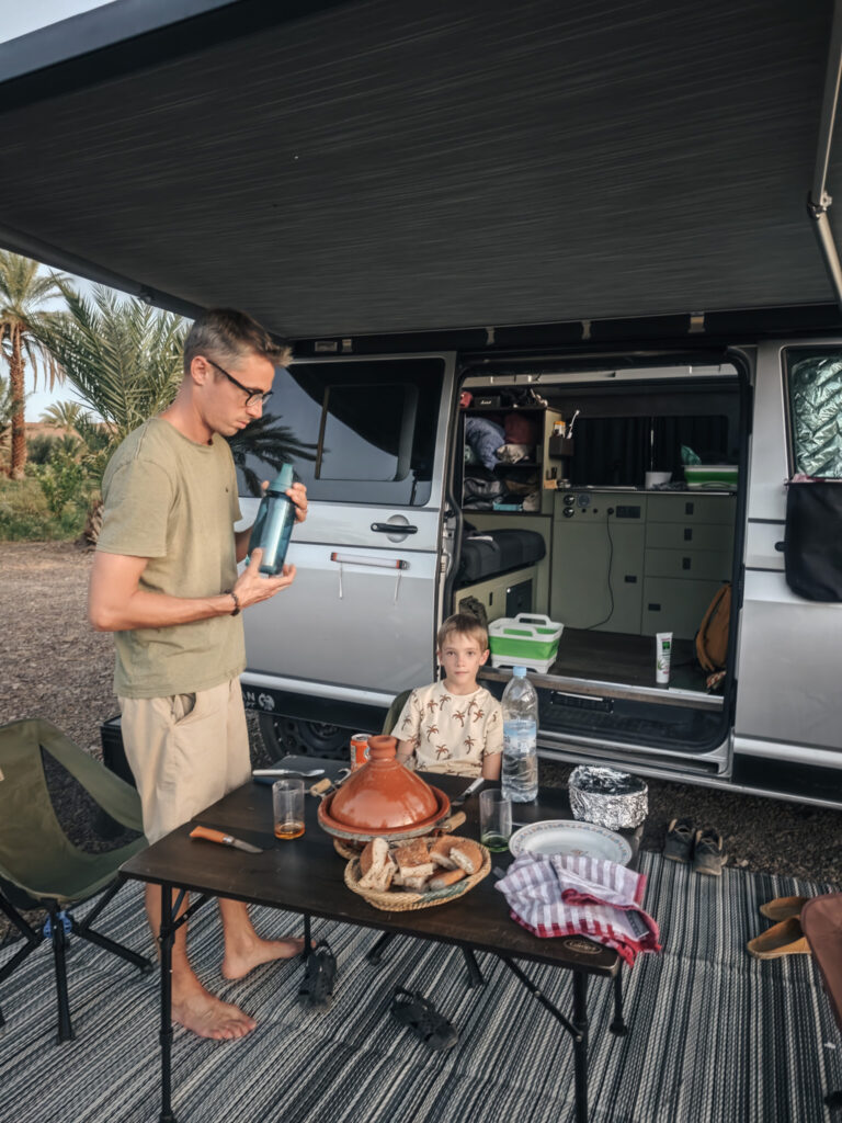 Tajine et panier de pain sur une table devant le van, avec un adulte et un enfant sous le store